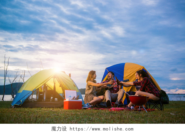 男人和女人享受露营野餐组的男人和女人享受露营野餐和烧烤在帐篷中背景的湖。年轻混合种族亚洲女人和男人。年轻人们手里烘培和欢呼瓶啤酒.